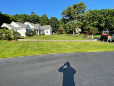 A large white house with a well-maintained lawn and two people near vehicles.