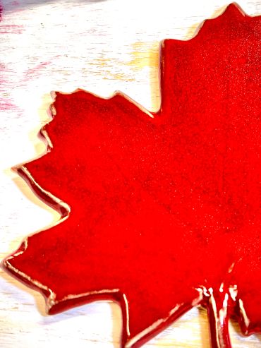 Close-up of a glossy red maple leaf-shaped ceramic piece.