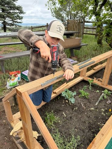 AJ using a drill on the garden boxes at Skyfall Ranch
