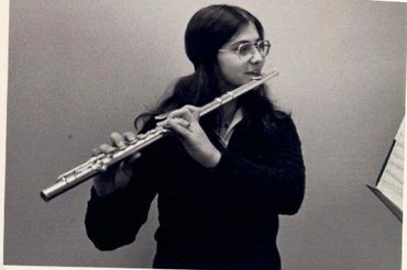 A black and white photo of a student with long hair and glasses, playing the flute