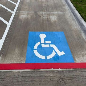 Handicap parking space with a blue symbol on concrete near a red curb.