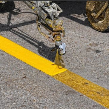Close-up of a machine spraying yellow paint on asphalt for road marking.