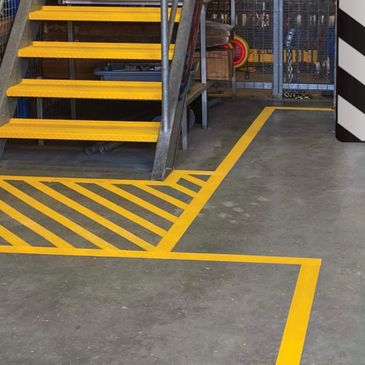 Industrial yellow safety markings near metal stairs on concrete floor.