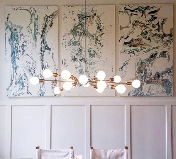 Modern chandelier with abstract art panels on a white paneled wall.