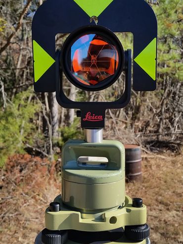 Surveying instrument with Leica branding outdoors in a wooded area.