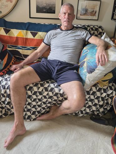 Man relaxing on a patterned couch surrounded by colorful pillows.