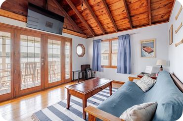 Cozy living room with wooden ceiling, blue curtains, and lake view through glass doors.