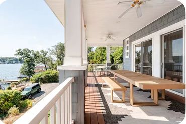 Spacious porch overlooking a lake with wooden table and bench seating.