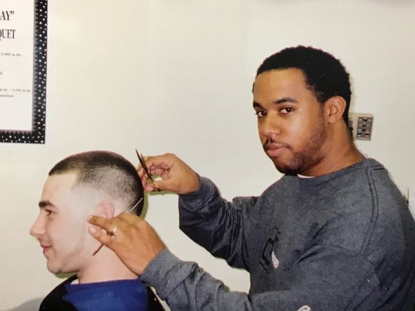 A man cutting another man's hair with scissors in a barbershop.