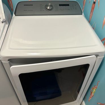 White Samsung front-load dryer with a tinted glass door in a colorful laundry room.