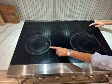 Two hands pointing at different burners on a glass stovetop.