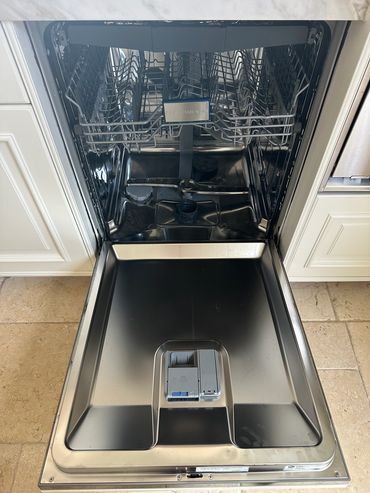 Open stainless steel dishwasher with empty racks and detergent compartments.
