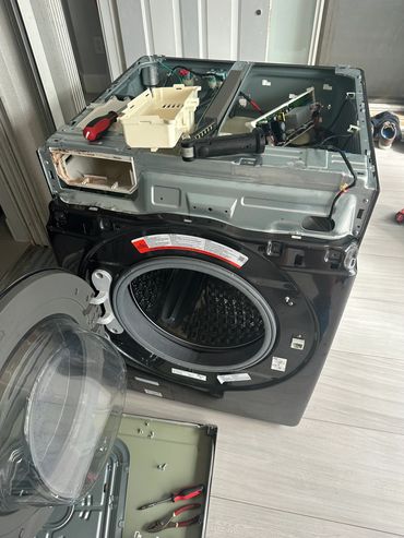 Disassembled front-loading washing machine with tools around it.