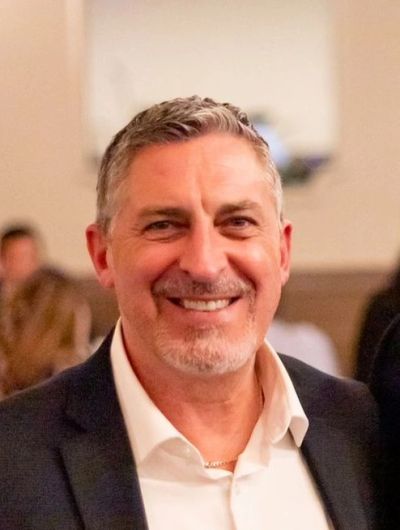 Smiling middle-aged man in a suit jacket at an indoor event.