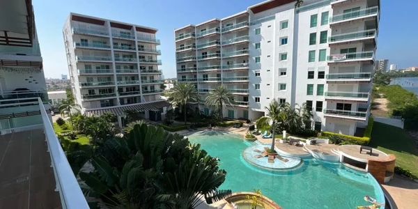 Modern apartment buildings surrounding a pool with palm trees under a clear sky.