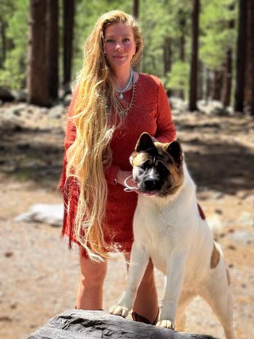 Woman with long hair in a red dress standing with a large dog outdoors.
