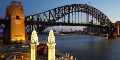 Sydney Harbour Bridge illuminated at dusk with city skyline and Opera House.