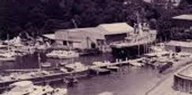 A historic black and white photo of a water reservoir and boats near a riverbank.