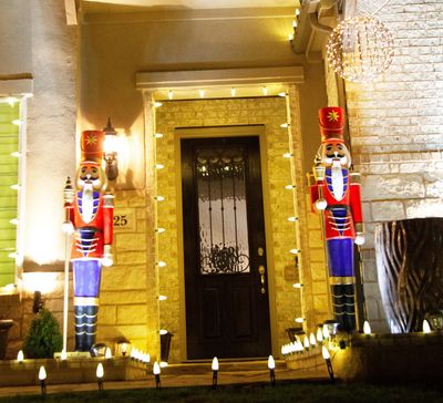 Two large illuminated nutcracker soldiers flank a front door decorated with lights.