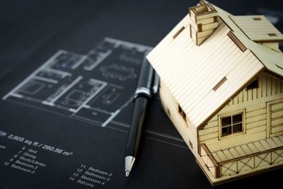 Wooden house model with floor plan and pen on blueprint.