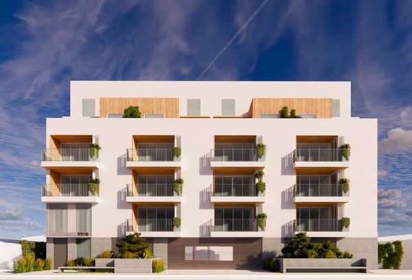Modern white apartment building with balconies and greenery under a blue sky.