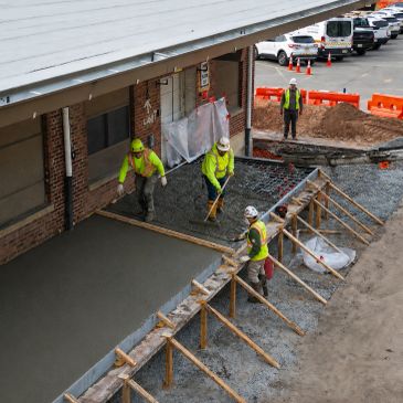 Construction workers pouring concrete near a building.