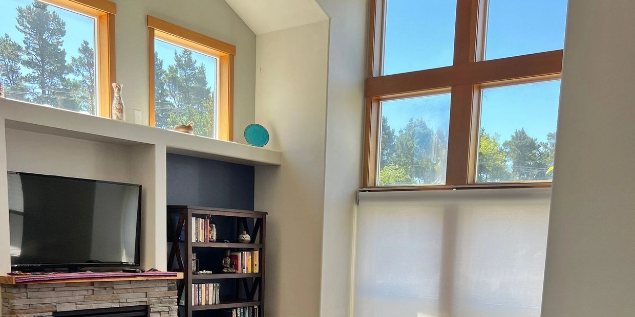 Bright living room with large windows, TV, and bookshelf.