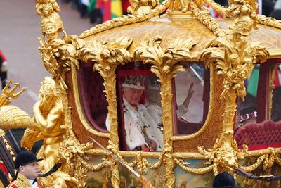 King Charles III and Queen Camilla in a golden royal carriage during a ceremonial procession.