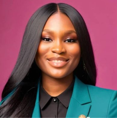 Professional woman smiling with long hair and teal blazer against pink background.