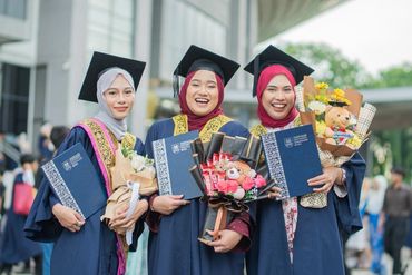 Graduates posing with diplomas and bouquets