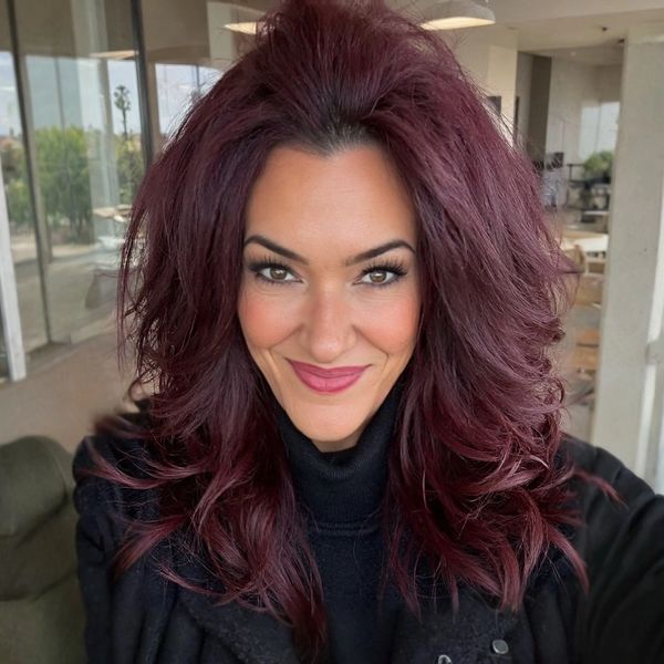 Woman with voluminous burgundy hair smiling indoors.