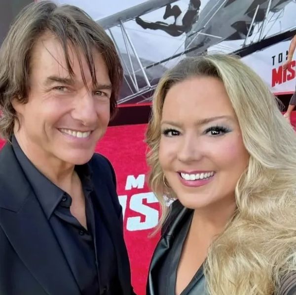 Two people smiling on a red carpet event with a movie poster background.