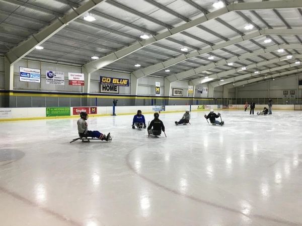 Participants in an ice arena learning how to play sled hockey.