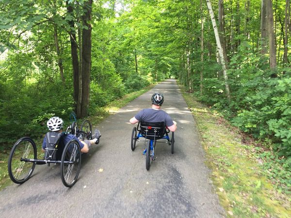 Two men handcycling down a paved park trail.
