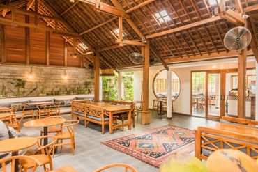 Cozy café with wooden furniture and a vibrant rug under a high wooden ceiling.