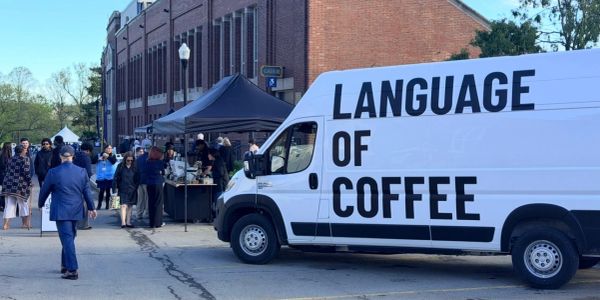White van with "Language of Coffee" at an outdoor market.