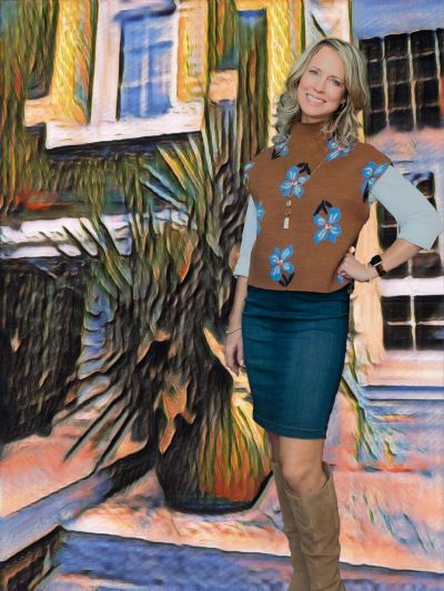 A woman smiling, dressed in a floral sweater and denim skirt, standing outdoors.