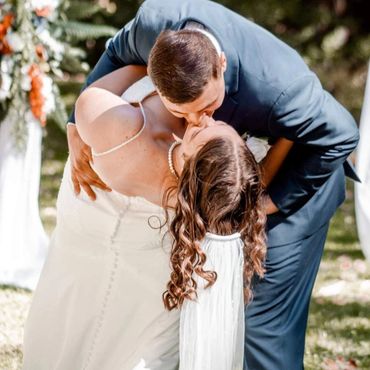 Bride and groom share a romantic kiss during their outdoor wedding ceremony.