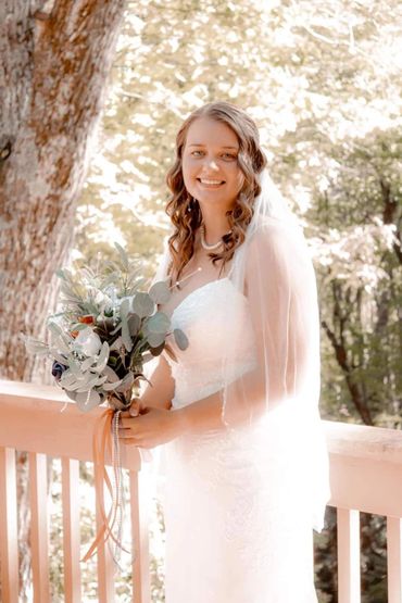 A smiling bride in a white wedding dress holding a bouquet outdoors.