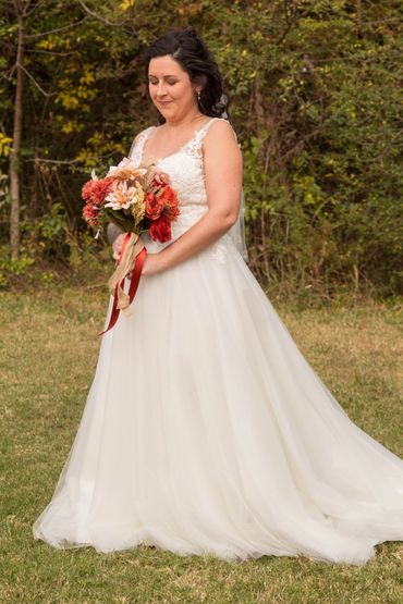 Bride in white dress holding a bouquet with autumn flowers.