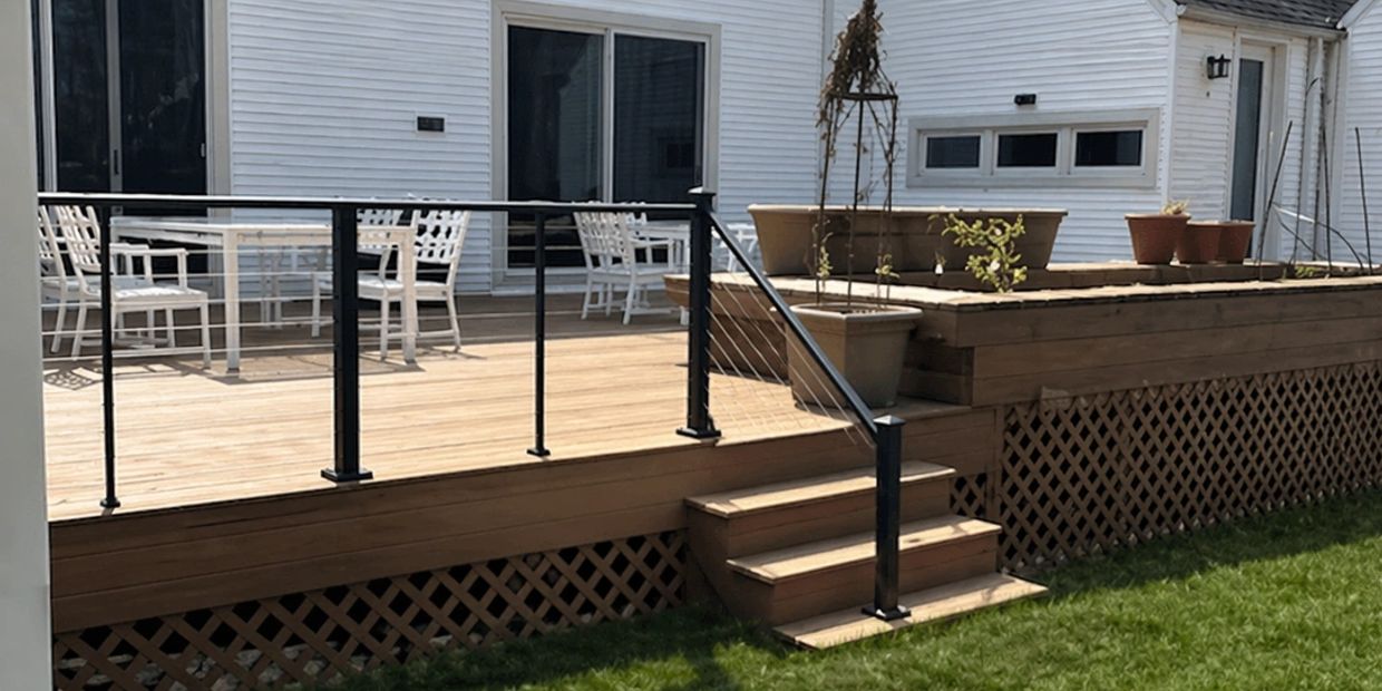A wooden deck with black railing and white patio furniture outside a white house.
