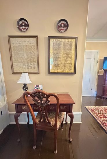 Vintage wooden desk and chair with framed historical American documents on the wall.