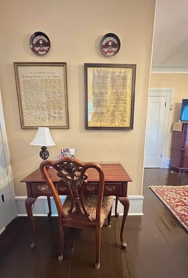 Vintage wooden desk and chair with framed historical American documents on the wall.
