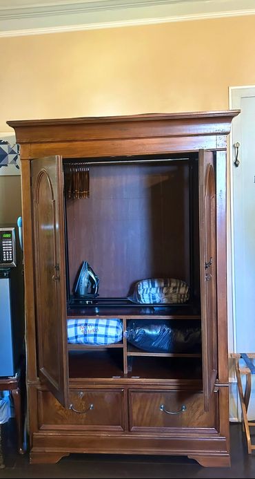 Open wooden armoire with blankets and an iron inside.