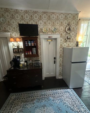 A cozy kitchen corner with a fridge, coffee station, and vintage wallpaper.