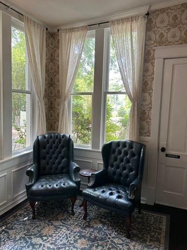 Two dark leather armchairs by curtained windows in a vintage room.