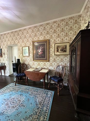 Classic dining room with vintage wallpaper, wooden furniture, and a blue patterned rug.