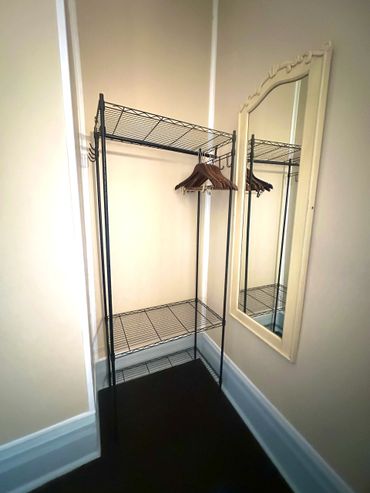 Metal clothing rack with wooden hangers next to a decorative mirror in a corner.