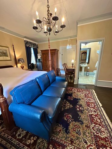Cozy bedroom with blue leather sofa, traditional wooden furniture, and chandelier.