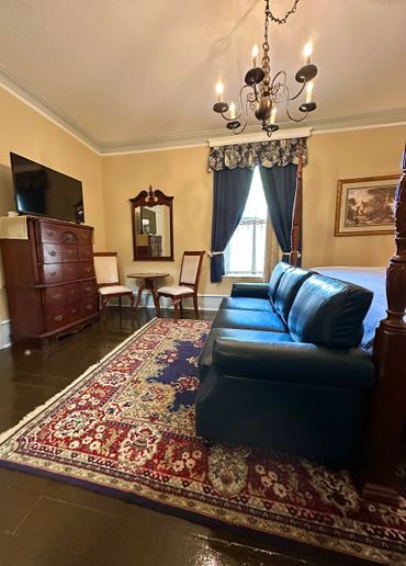 A cozy vintage-style living room with classic furniture and a chandelier. Elegant Room 1 with a four-poster bed and blue leather couch in room private Bathroom.